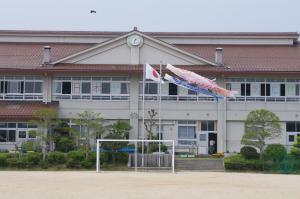 小学校の校舎とグラウンドと鯉のぼりと日本の国旗の写真