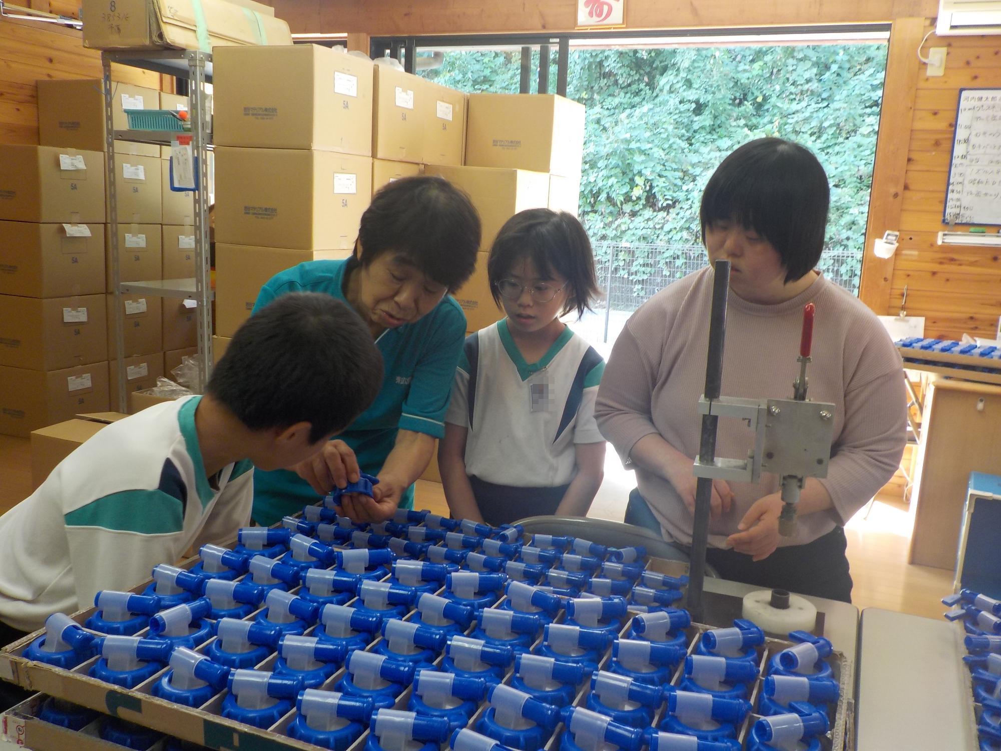 つばさの利用者さんと一緒に仕事の内容を聞く児童たち