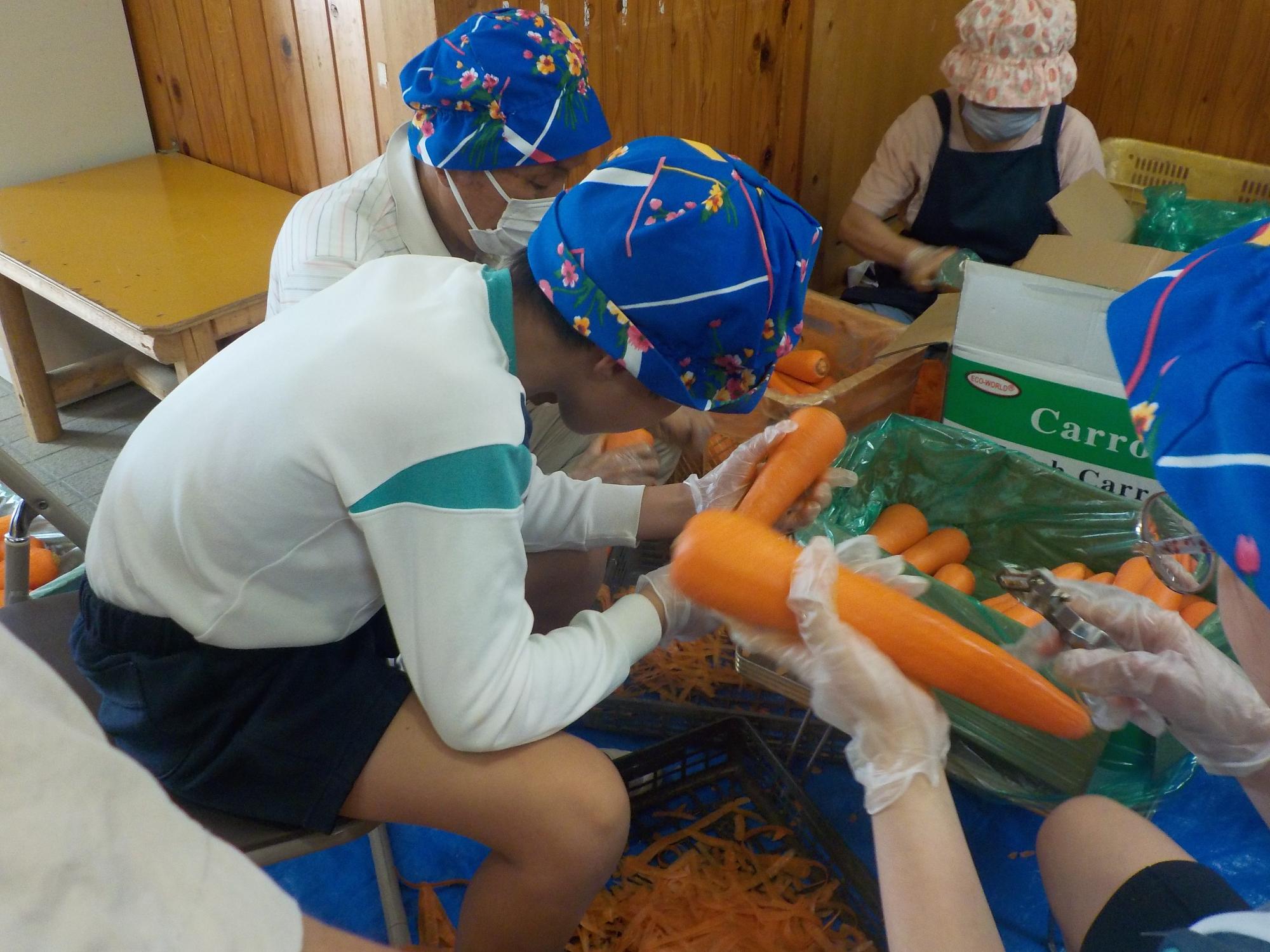 おそろいの頭巾をかぶって人参の皮をむく様子