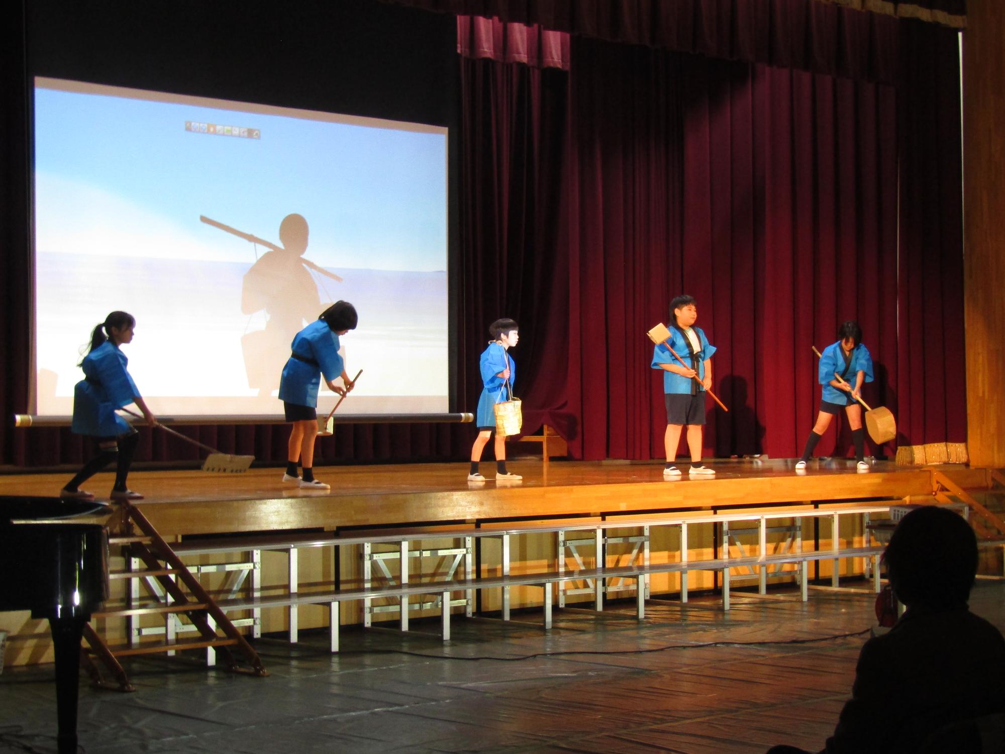 青い法被を着て塩づくりの作業の様子を再現する子供たち