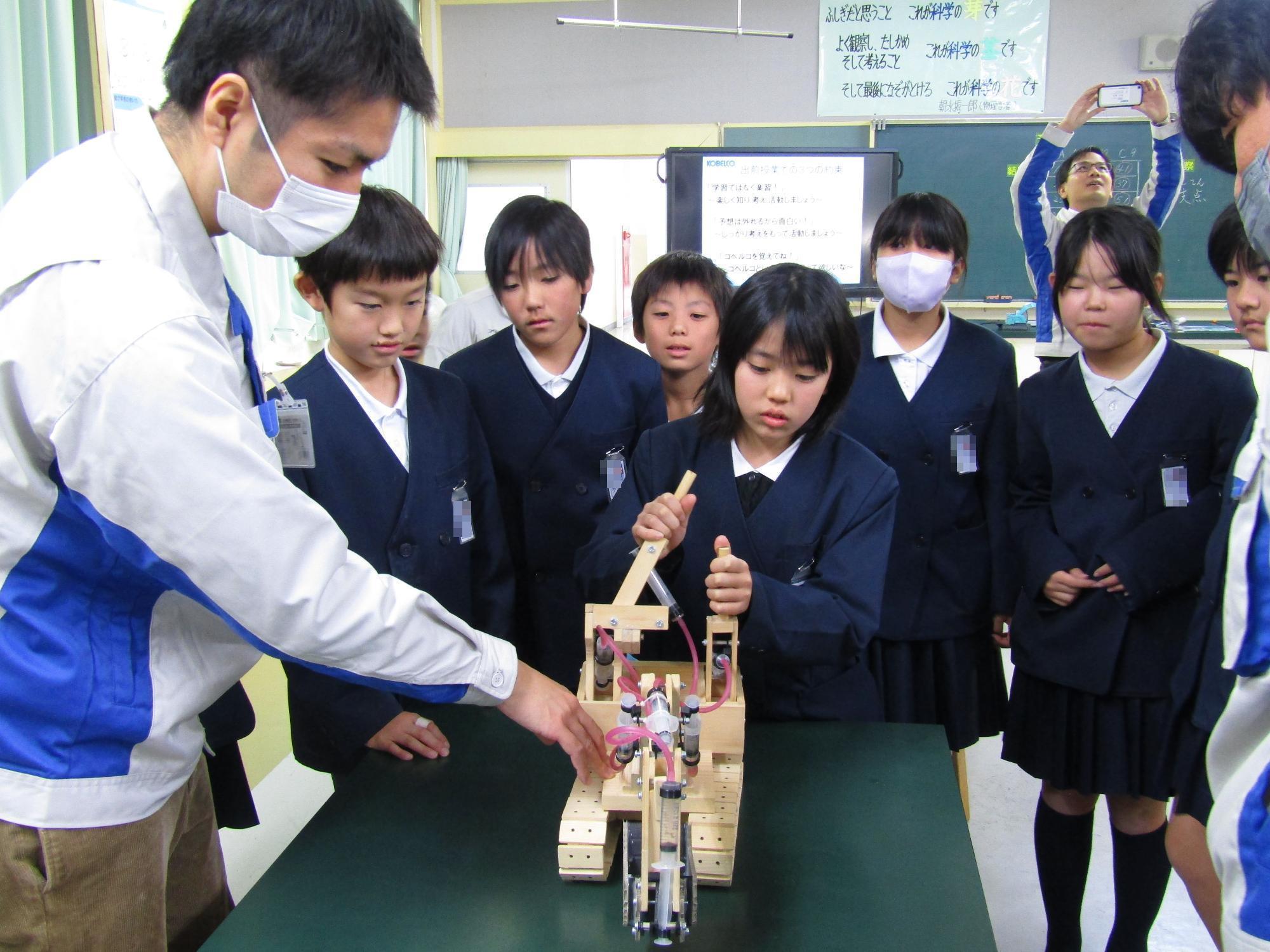 木製のミニチュアショベルカーを操作する女子児童