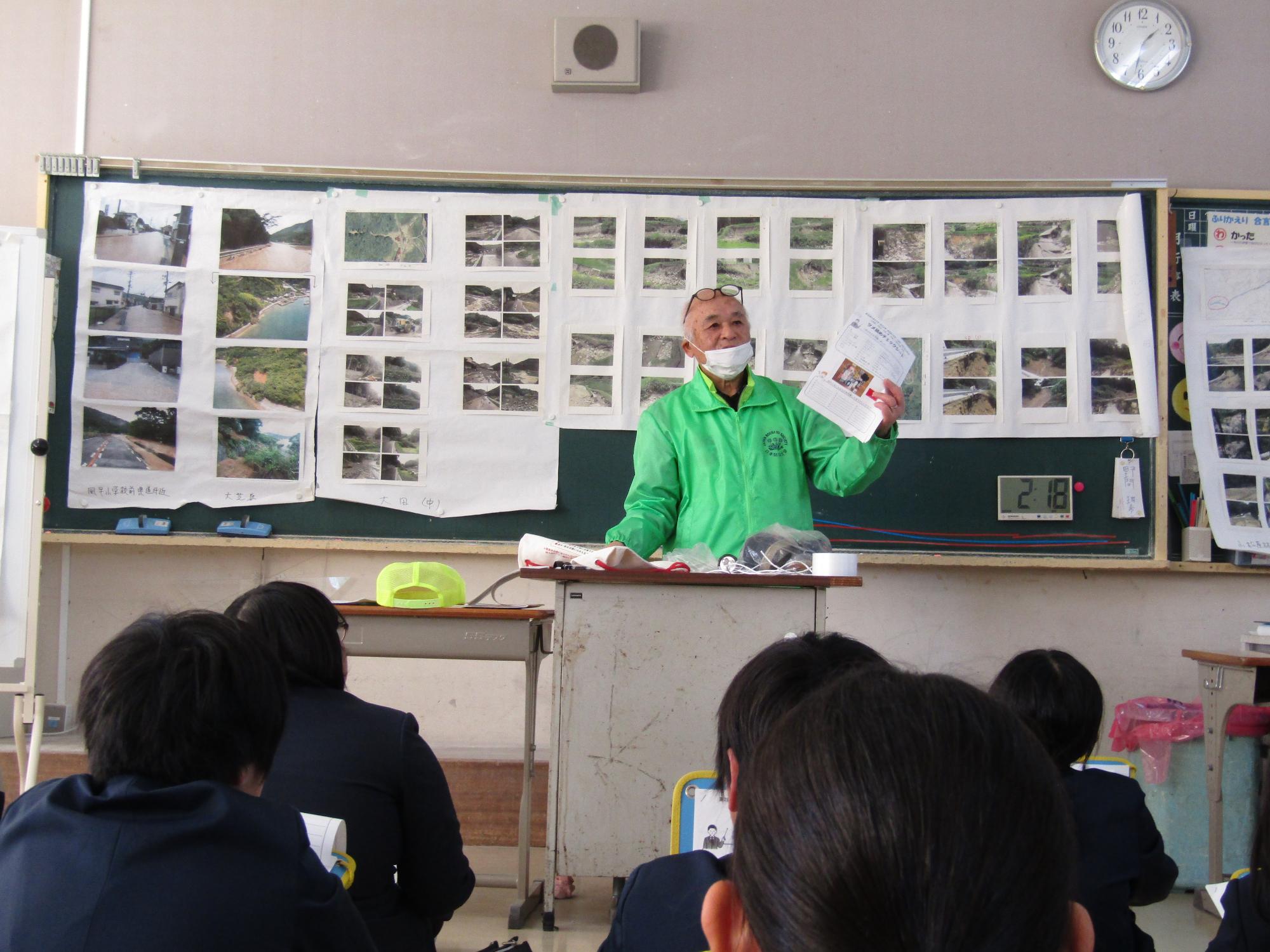 たくさんの写真を背景に話をする防災士