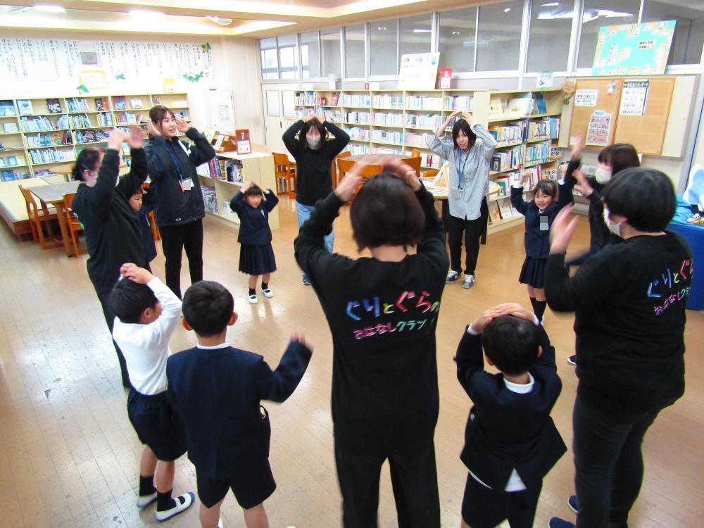 輪になって体を動かす児童と読み聞かせボランティアさんたち