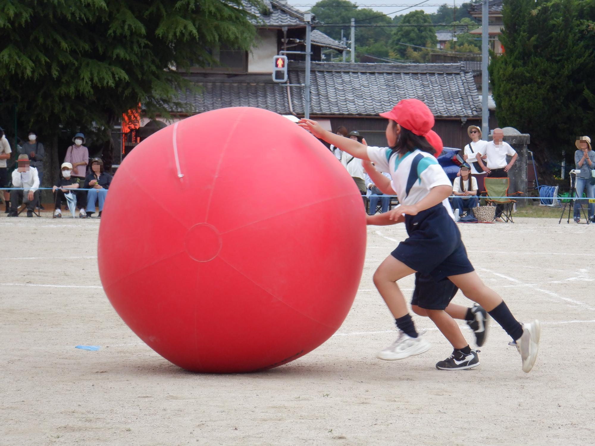 赤い大玉を転がす児童