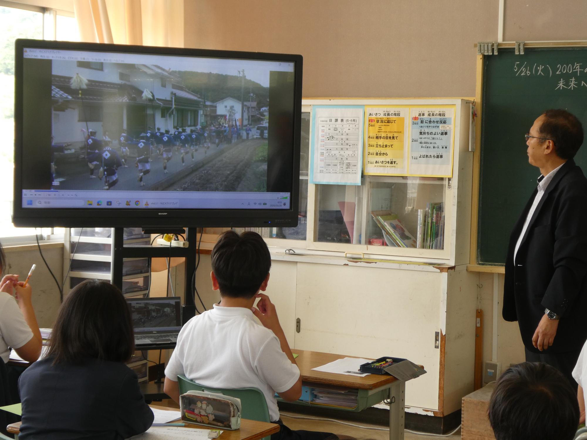 電子黒板に映る神賑行列の写真を見る宮司さんと児童