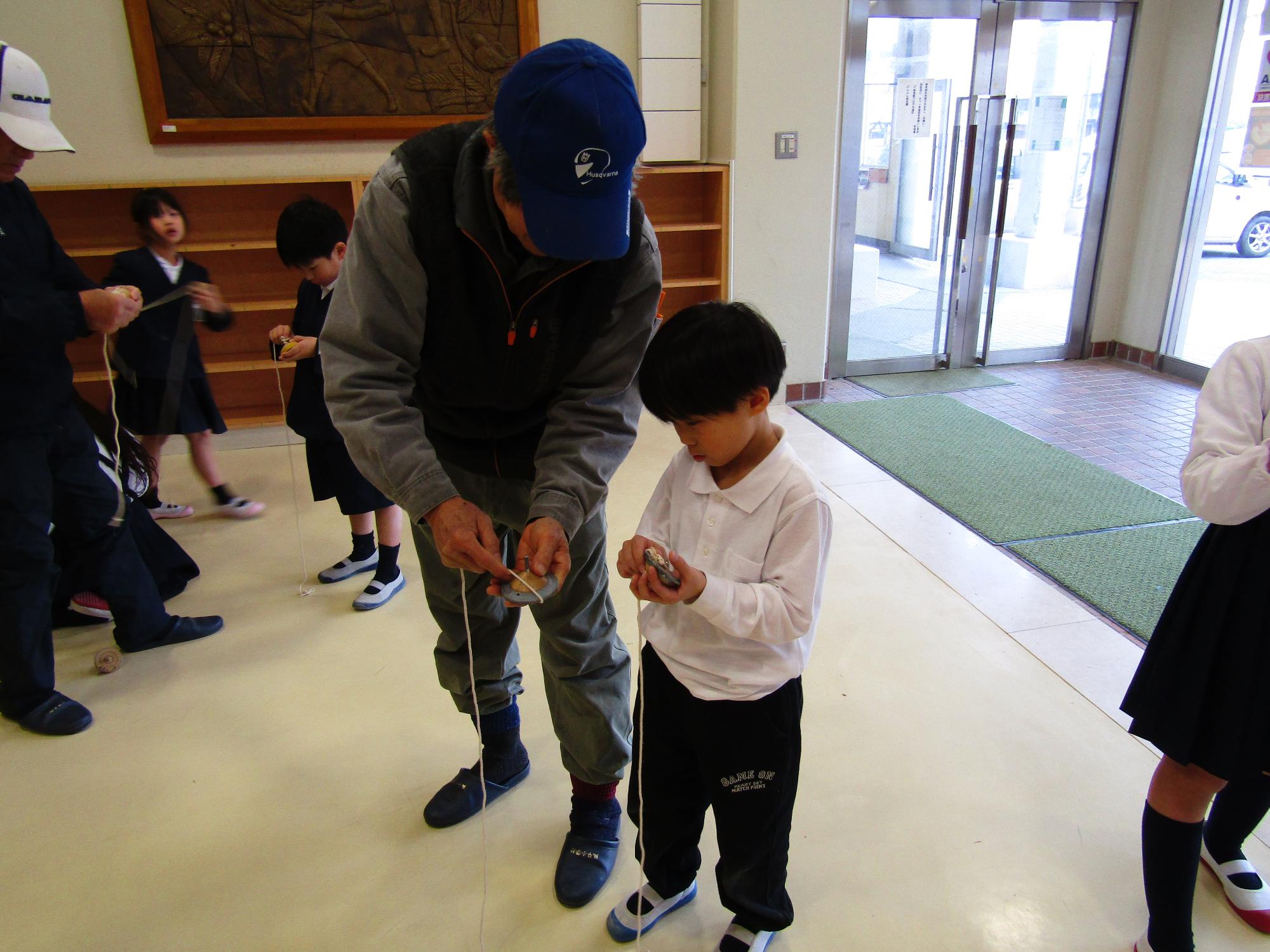 こまにひもをかける方法をアドバイスする男性と教わる男子児童