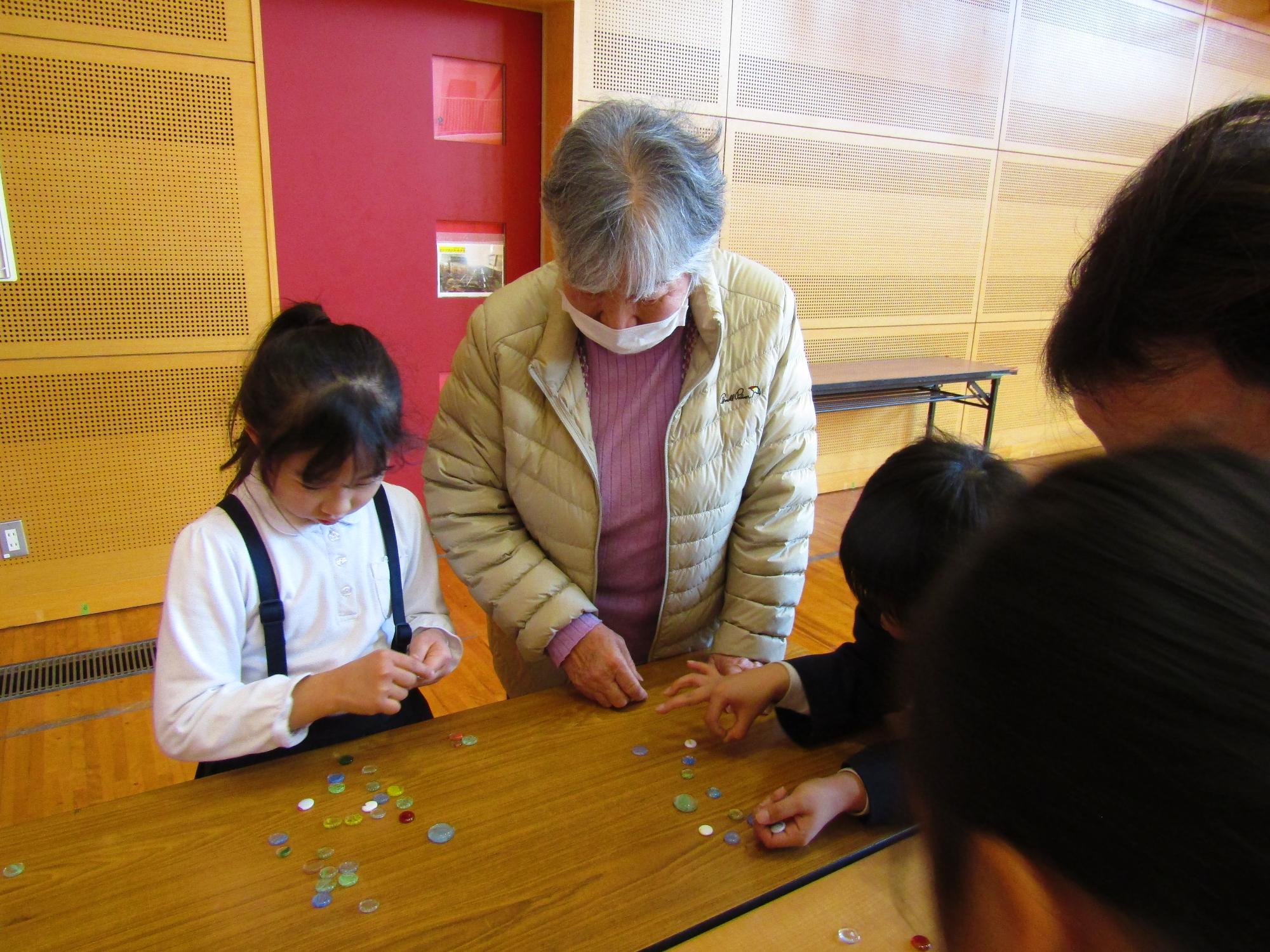 おはじきであそぶ女子児童と女性
