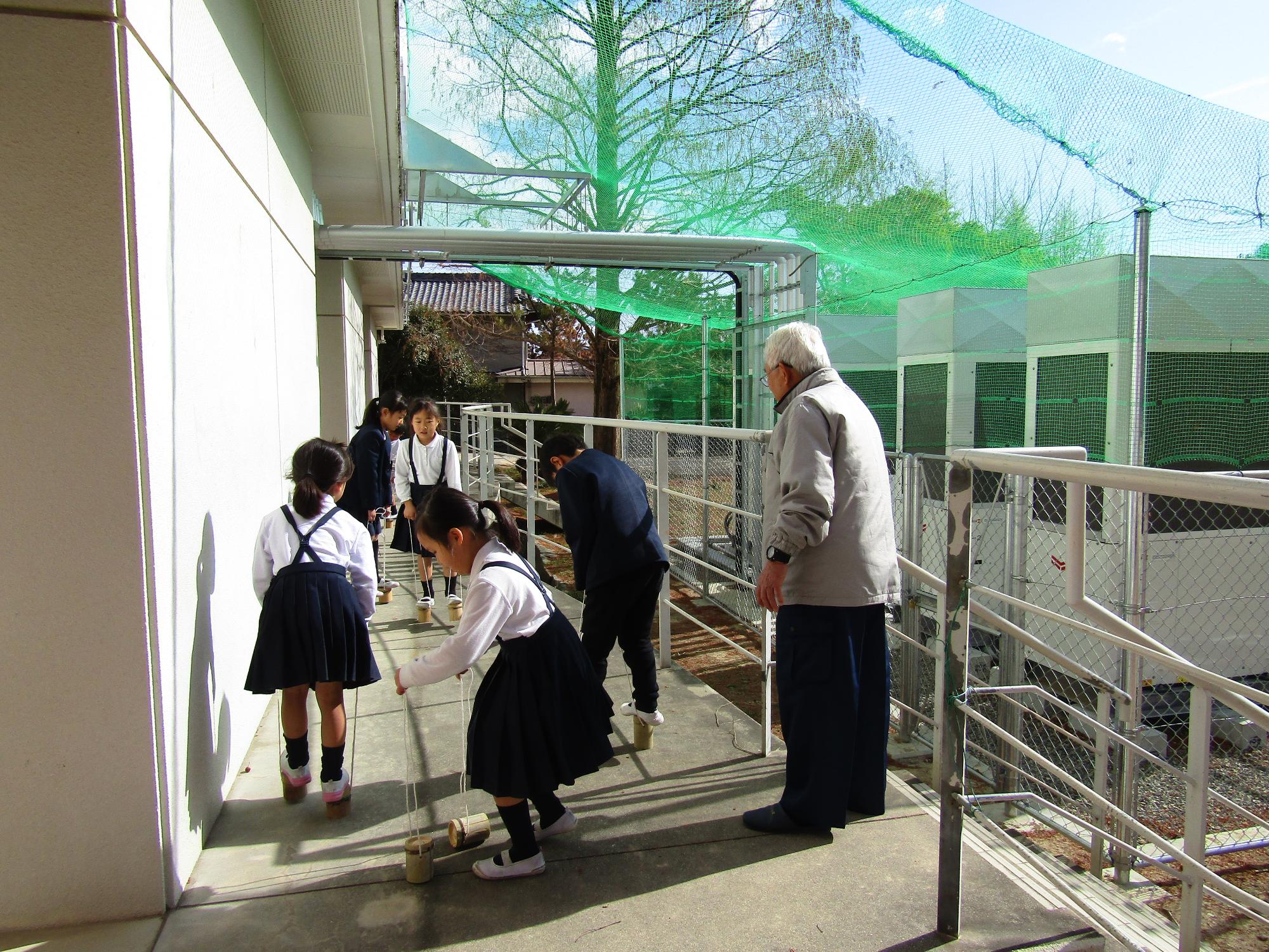 竹ぽっくりで遊ぶ子供たちと見守る男性