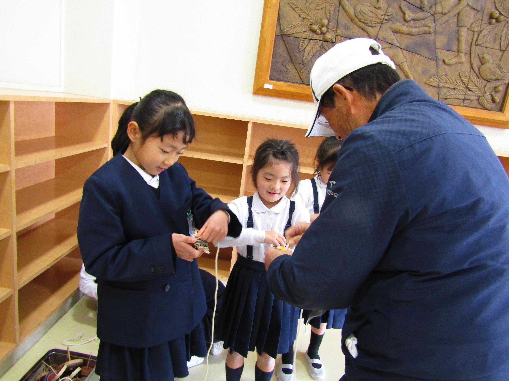 こまにひもをかける方法を聞く女子児童たち