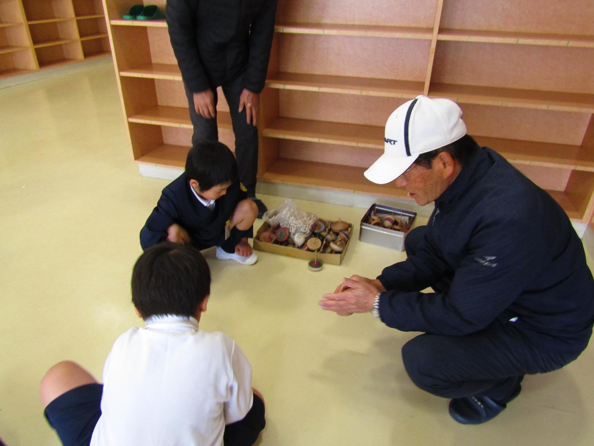 こまの軸を回して遊ぶ男子児童たちと男性