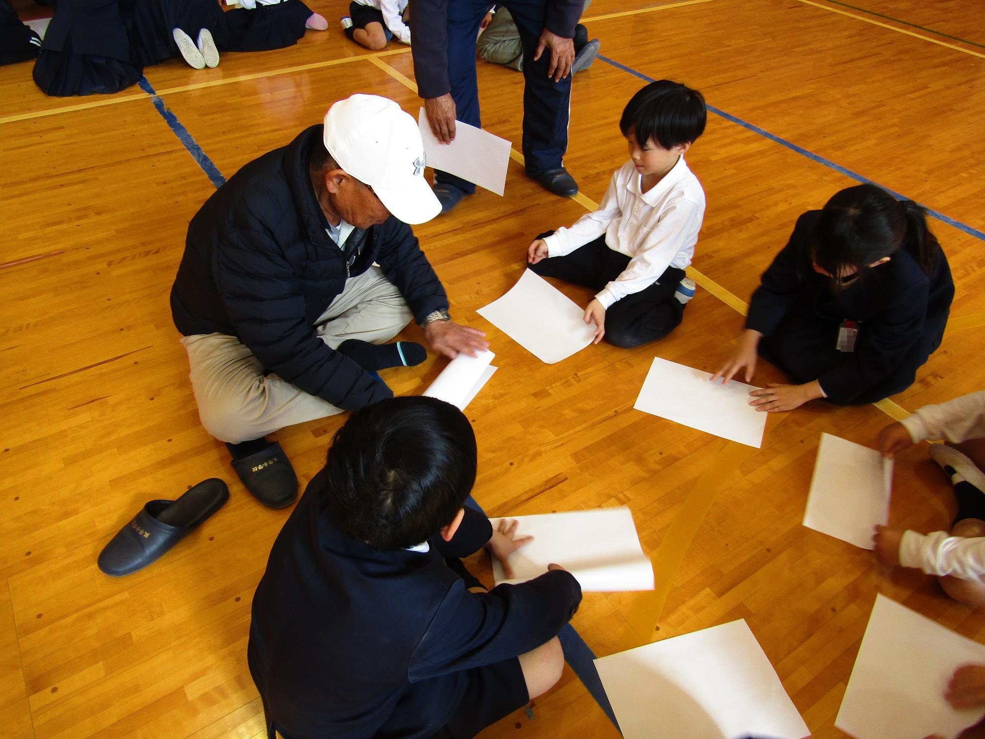 班に分かれて紙飛行機の折り方を教わる子供たち