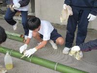 門松づくりで軍手を付けて竹に油を塗っている生徒